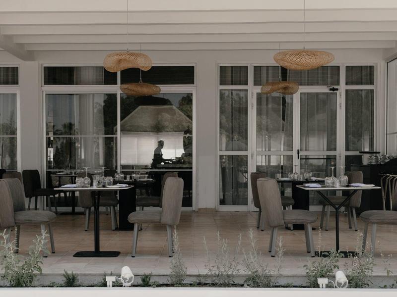 Moderner Außenbereich eines Cafés mit grauen Stühlen, runden Tischen und großen Fenstern.