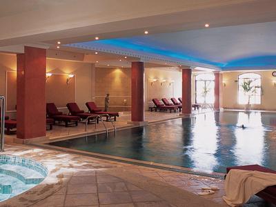 Innenbereich mit Schwimmbad, Whirlpool, Liegestühlen und großen Fenstern für Tageslicht.