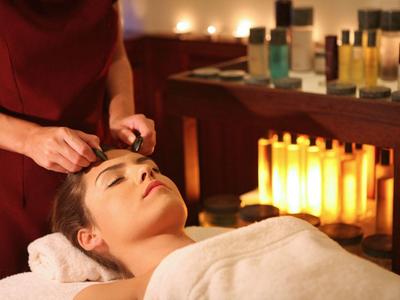 Frau entspannt beim Gesichtsmassage in ruhigem, warm beleuchtetem Wellnessraum mit Kerzen und Pflegeprodukten.