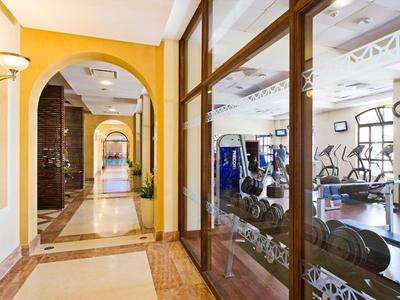 Chodba se žlutými stěnami vedle hotelové posilovny s prosklenými stěnami.