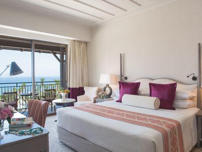 Hell eingerichtetes Schlafzimmer mit großem Bett, Balkon und Meerblick bei Tageslicht.