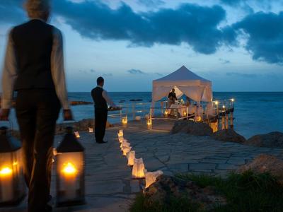 Abendliche Strandszene mit Kerzenlichtern, Personen tragen Laternen und ein Pavillon im Hintergrund.