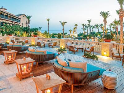 Luxuriöse Terrasse mit gemütlichen Rundsofas, Holzmöbeln und Palmen bei Dämmerung.