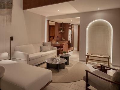 Nowoczesny pokój hotelowy z beżową sofą, okrągłymi stolikami i pośrednim oświetleniem.