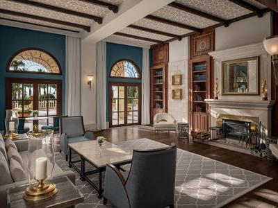 Elegancki salon hotelowy z fotelami, kominkiem i dużymi oknami wpuszczającymi dużo światła dziennego.