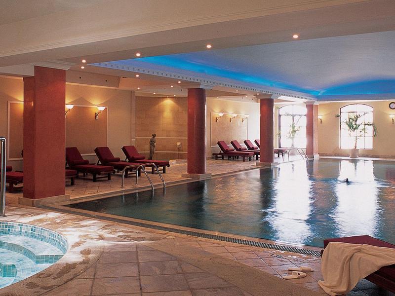 Innenbereich mit Schwimmbad, Whirlpool, Liegestühlen und großen Fenstern für Tageslicht.