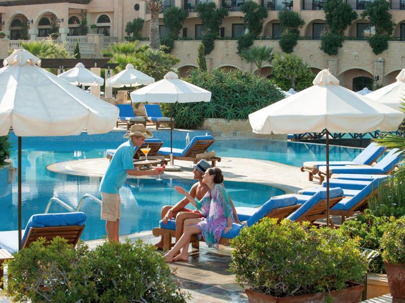 Hotelpool mit Liegestühlen, Sonnenschirmen und Menschen in entspannter Atmosphäre im Außenbereich.