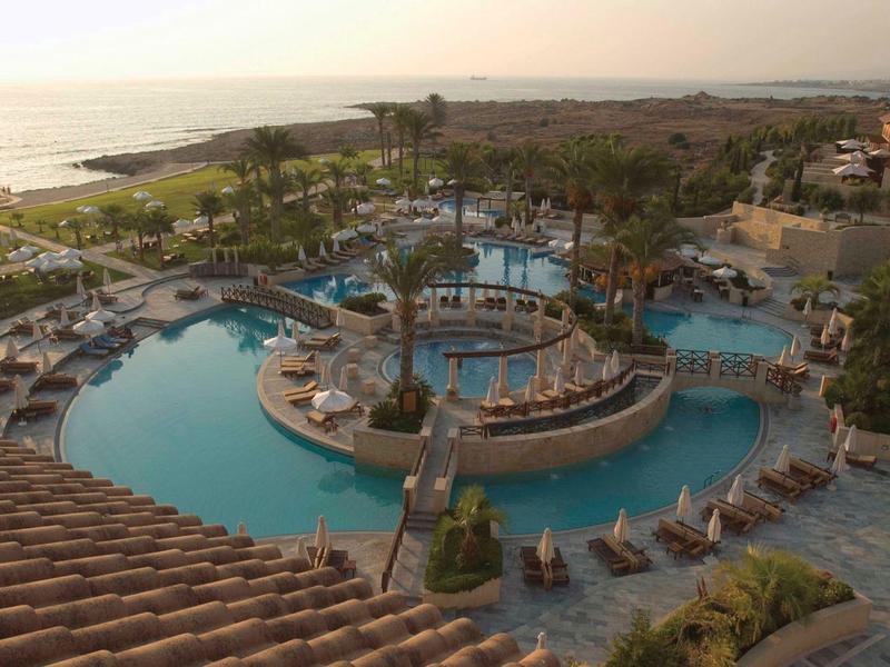 Großer Pool mit Insel, Sitzbereich und Liegestühlen an Küste bei Sonnenuntergang.