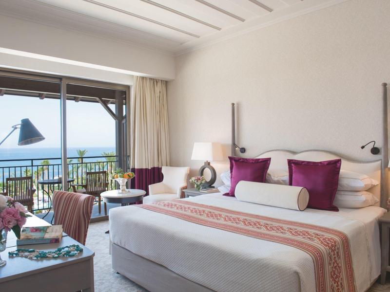 Hell eingerichtetes Schlafzimmer mit großem Bett, Balkon und Meerblick bei Tageslicht.