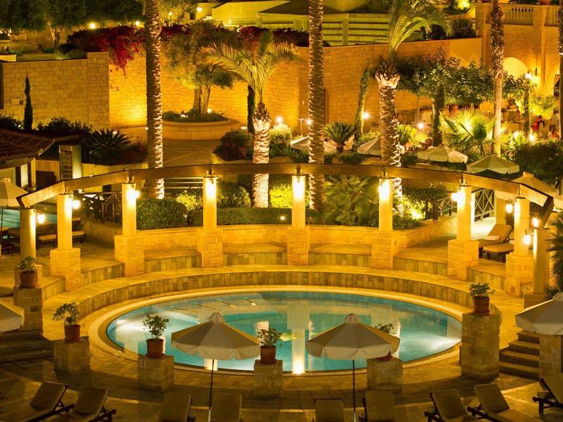 Ein beleuchteter Pool mit Palmen und Liegestühlen in einer warmen, einladenden Nachtatmosphäre.