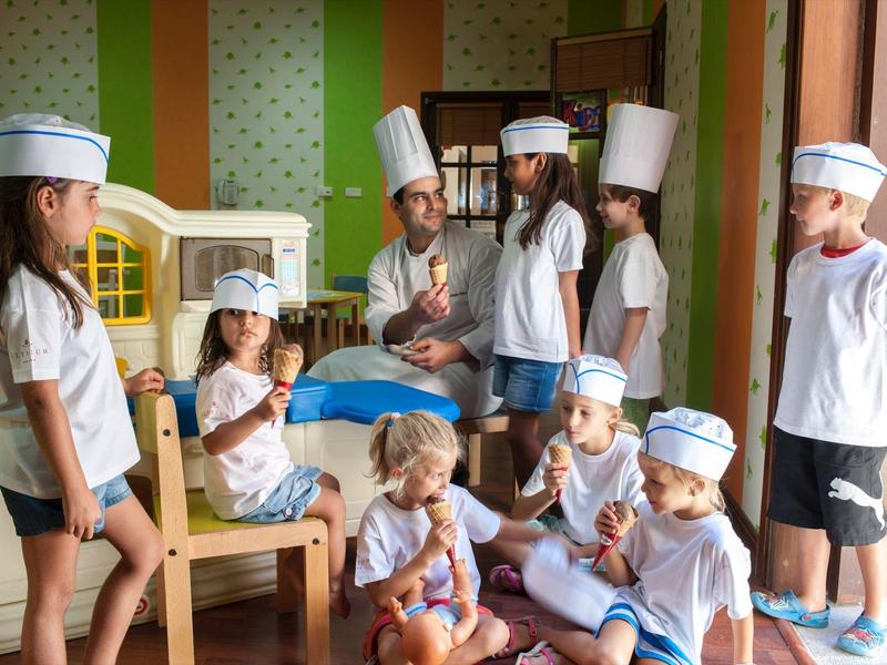 Kinder in weißer Kochkleidung spielen gemeinsam in einem hellen Raum mit Holzmöbeln.