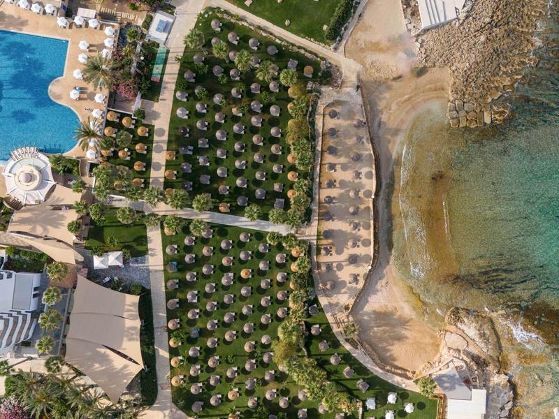 Luftaufnahme eines Küstenresorts mit Pool, Palmen, Sandstrand und klarem türkisfarbenem Wasser.