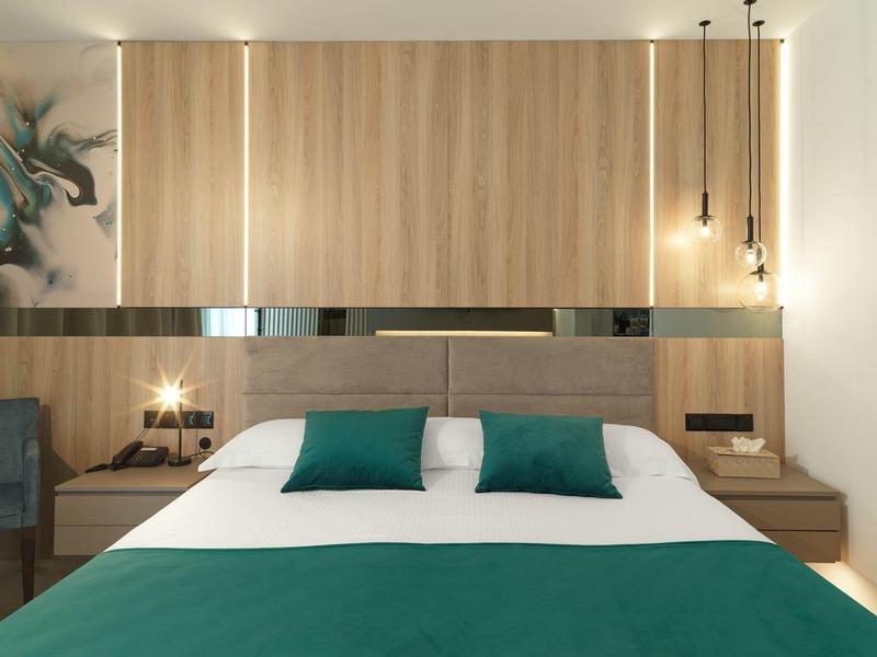 Modernes Schlafzimmer mit großem Bett, grünem Bettzeug, Holzpaneelen und Hängeleuchten.