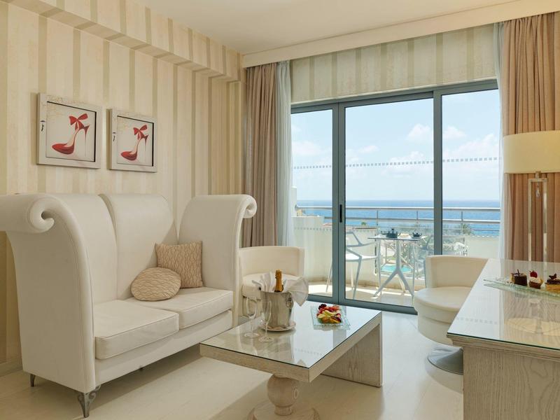 Helles Wohnzimmer mit weißen Möbeln, Glastisch, maritimer Aussicht und sanfter Beleuchtung.