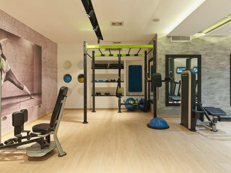 Moderner Fitnessraum mit Trainingsgeräten, Holzboden und großem Wandbild einer Sportlerin.