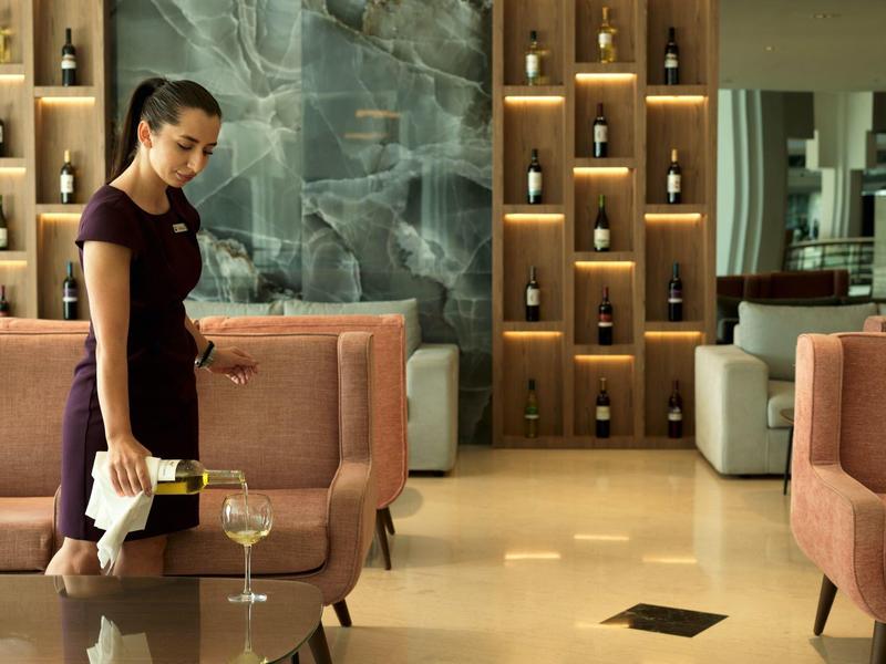 Eine Frau in dunkelrotem Kleid wischt einen Glastisch in einem modernen, elegant gestalteten Raum.