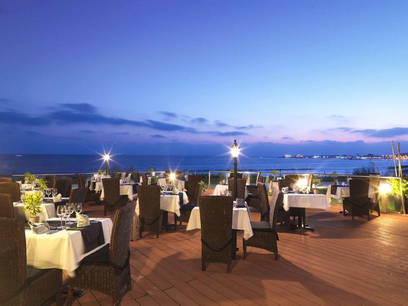 Abendliche Terrasse mit gedeckten Tischen und Stühlen, Blick auf den Meereshorizont und blauen Himmel.