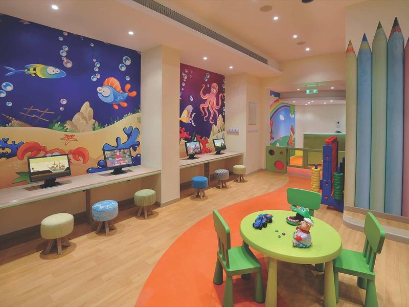 Bunter Kinderraum mit rundem Tisch, kleinen Stühlen, Wandbildern und spitz zulaufender Wanddeko.