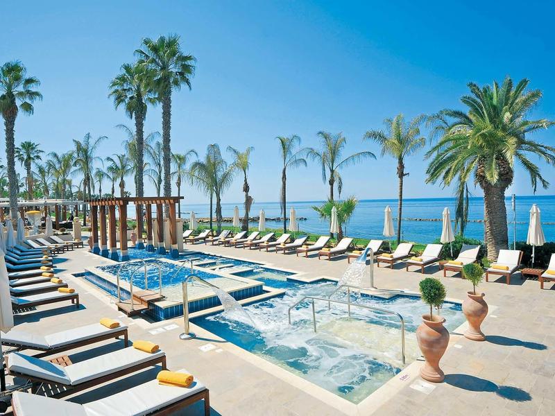 Luxuriöser Poolbereich mit Liegestühlen, Palmen und Blick auf das blaue Meer unter klarem Himmel.