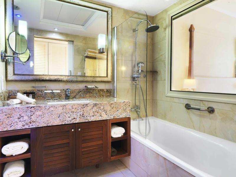 Helles Badezimmer mit Granitwaschbecken, Holzschränken, großer Spiegel und Badewanne mit Dusche.