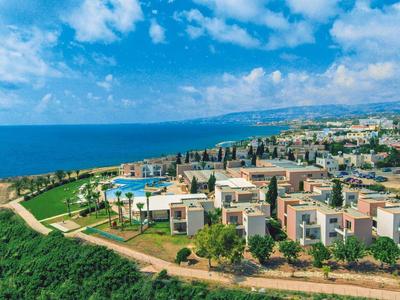 Blick auf eine Küstenstadt mit modernen Gebäuden, grünen Flächen und blauem Meer unter blauem Himmel.