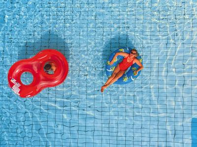Person entspannt sich auf einer Schwimminsel im blauen Pool mit Wasserfliesen.