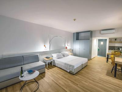Helles Hotelzimmer mit Doppelbett, grauem Sofa, Holzboden und modernem Schreibtischbereich.