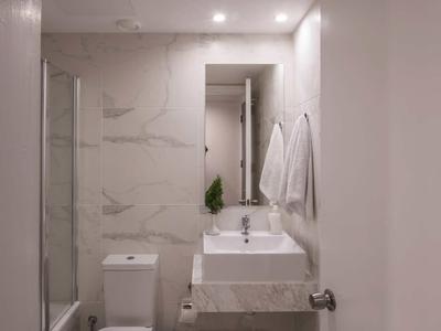 Kleines modernes Badezimmer mit weißer Toilette, Waschbecken, Spiegel und Handtüchern an der Wand.