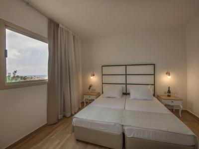 Schlichtes Schlafzimmer mit zwei Einzelbetten, Holzfußboden, Fenster und Vorhängen.