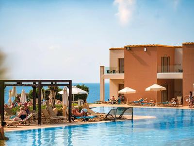 Moderner Hotelpool mit Gästen, die in Liegestühlen entspannen, und Blick auf das Meer im Hintergrund.