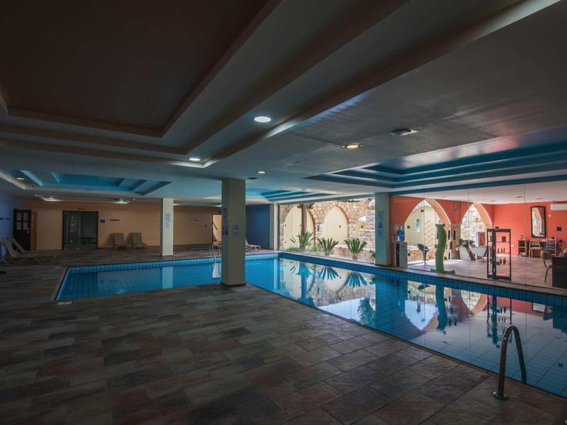 Großes Hallenbad mit Säulen, blauen Deckenakzenten und orangenen Wänden mit Fensterbögen.