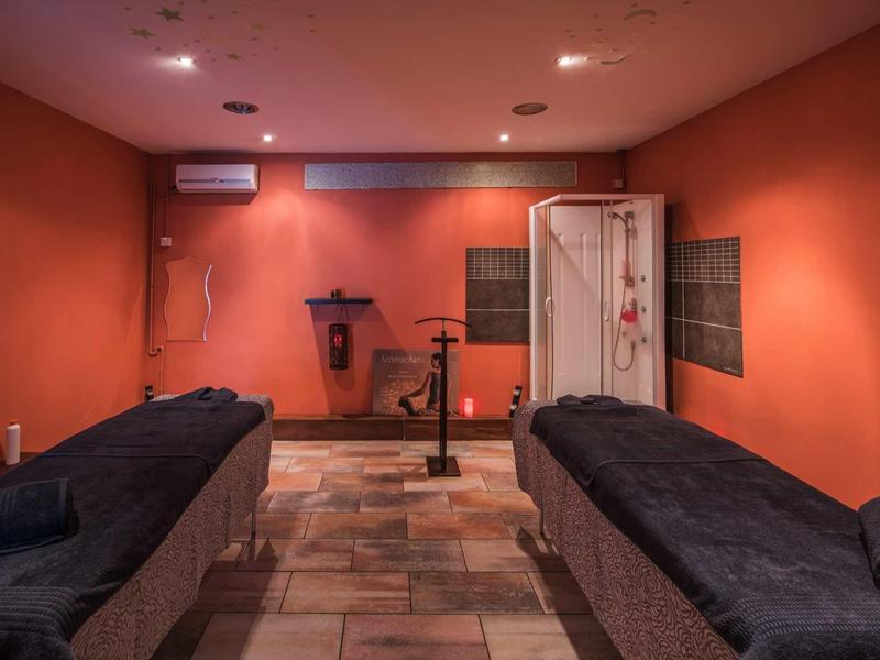 Ein ruhiger Massageraum mit zwei Behandlungsliegen, oranger Wandfarbe und gedämpftem Licht.