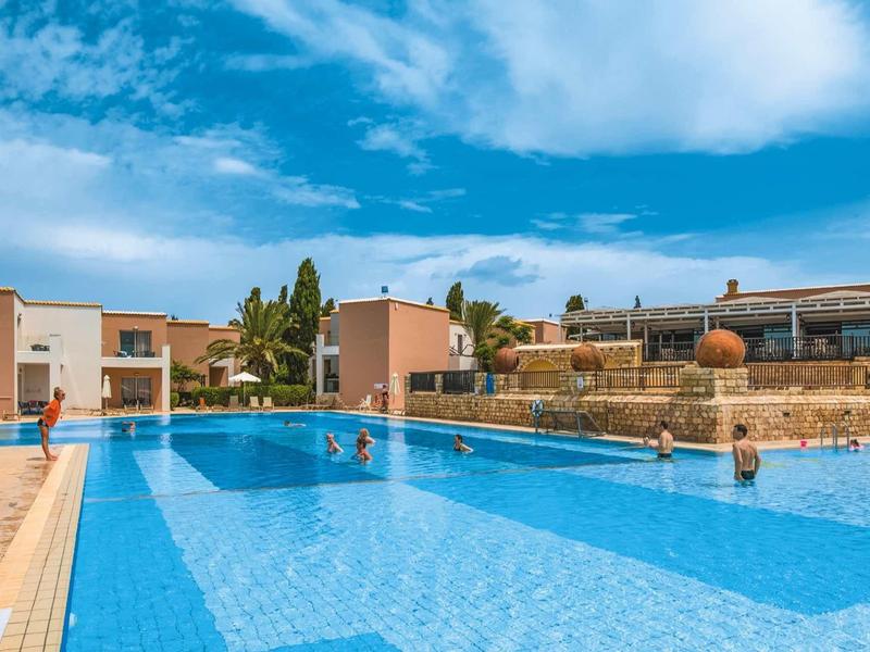 Großer sauberer Pool mit blauer Mosaikfliesen, umgeben von modernen Gebäuden und blauem Himmel.