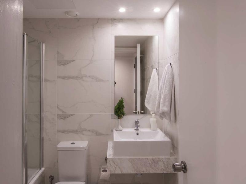 Kleines modernes Badezimmer mit weißer Toilette, Waschbecken, Spiegel und Handtüchern an der Wand.