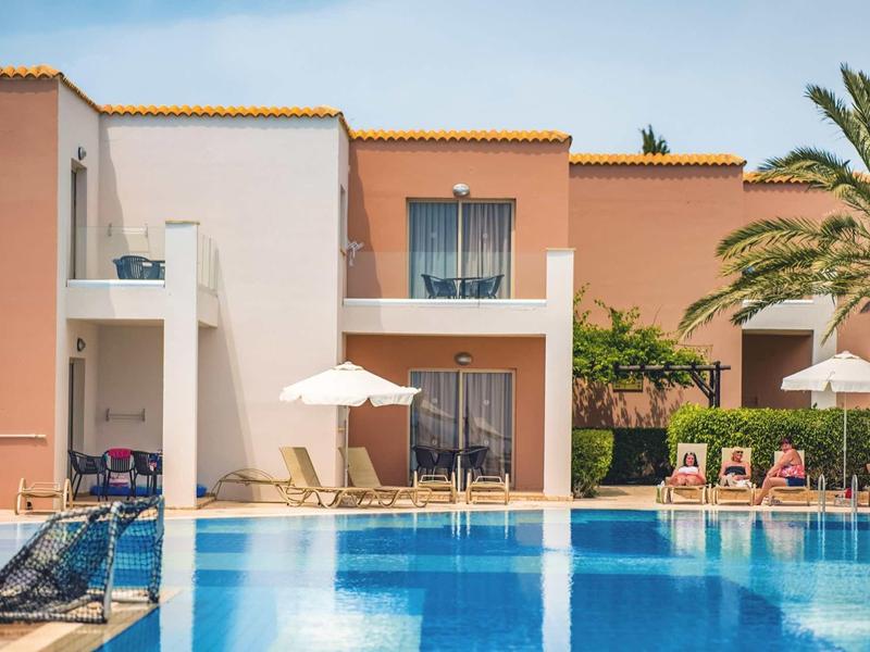 Wohnhaus mit Balkonen, Sonnenschirmen und Liegestühlen neben blauem Swimmingpool.