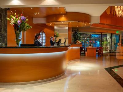 Modern hotel lobby with curved reception desk, flower arrangement, and spacious seating area.