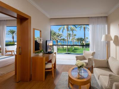 Modern hotel room furnished with view of palm trees and pool through large windows.