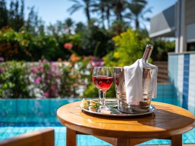 A drink and champagne cooler on a wooden table by the pool with plants in the background.