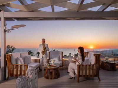 Two people enjoy the sunset on a stylish rooftop terrace with seating and ocean view.