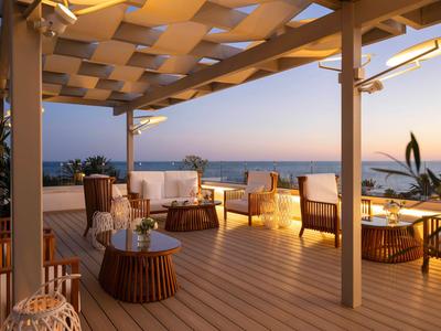 Cozy hotel terrace at sunset with sea view and modern wooden furniture.