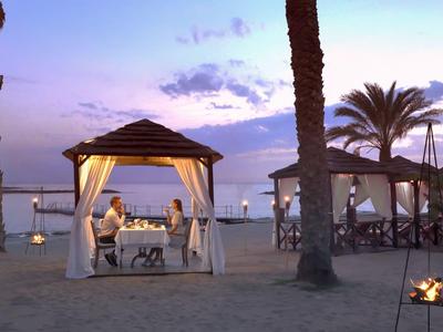 Evening beach gazebos with set tables among palm trees under a blue-purple sky.