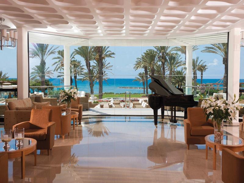 Luxuriöse Lounge mit braunen Sesseln, Flügelklavier und Meerblick durch große Fenster.