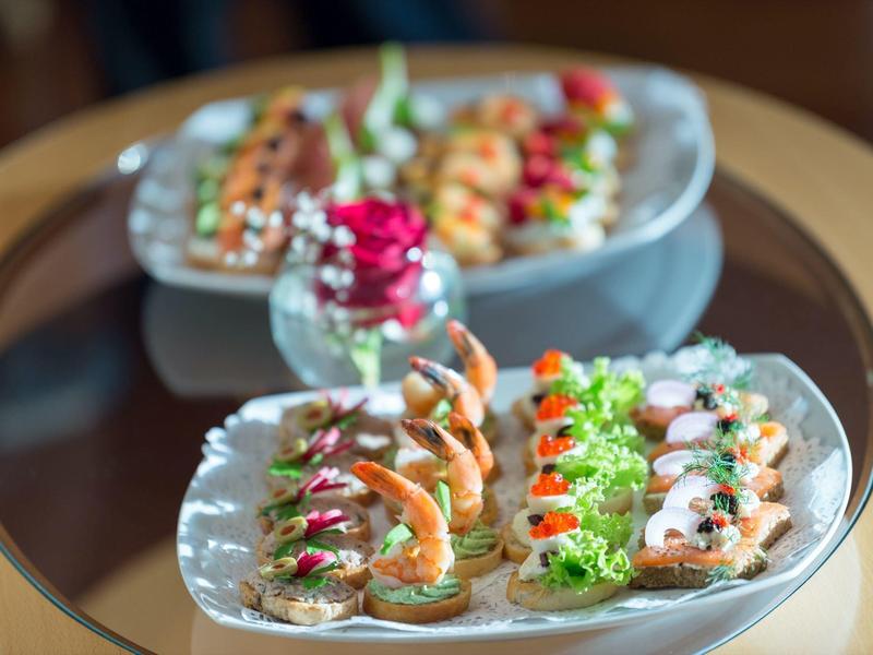 Zwei weiße Teller mit bunt belegten Canapés auf einem runden Glastisch, im Hintergrund Rosen.