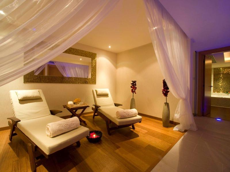 Gemütlicher Wellnessraum mit Holzboden, zwei Liegestühlen, sanfter Beleuchtung und weißen Vorhängen.