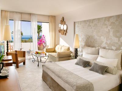 Lichte hotelkamer met groot bed, zithoek en balkon met uitzicht op zee.