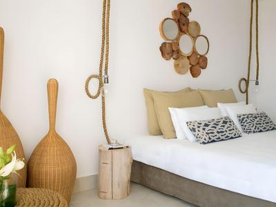 Camera d'hotel semplice con letto chiaro, cuscini, oggetti decorativi in legno e elementi naturali in legno.