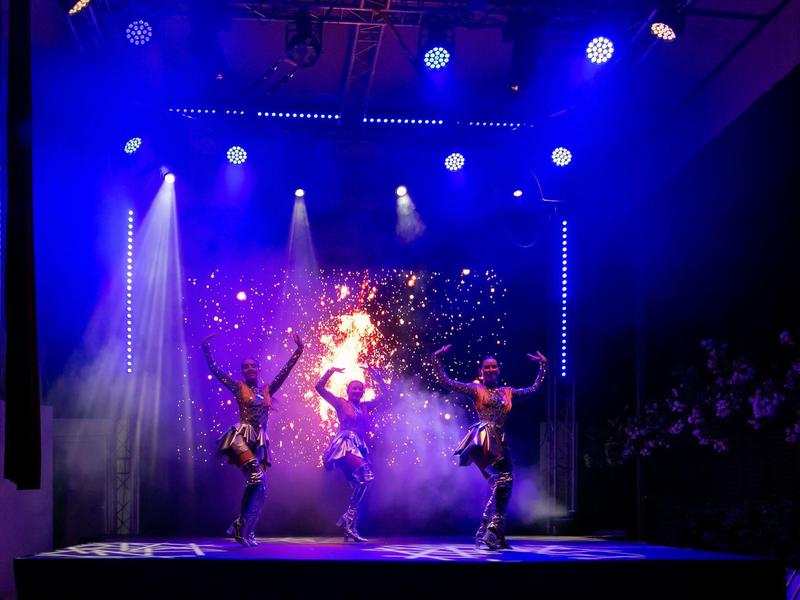 Drei Tänzerinnen in schwarzen Kostümen performen auf bühne mit blauem und lila Licht.