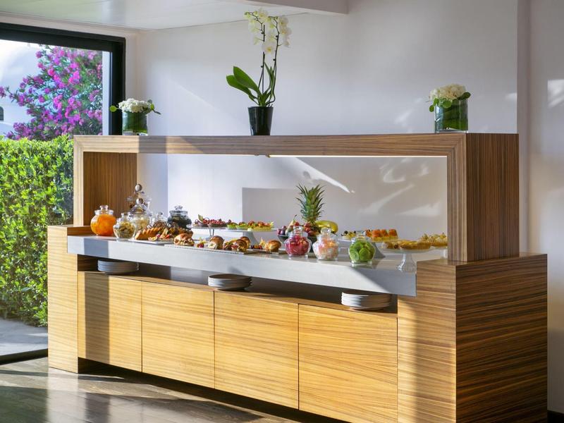 Moderner Buffet-Tisch mit Holzfront, Spiegelrückwand und vielfältigem Frühstücksbuffet in hellem Raum.