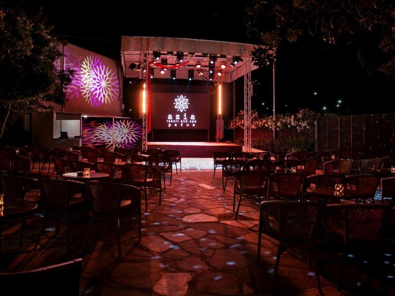 Dunkler Außenbereich mit Bühnenlicht, leeren Tischen und Stühlen bei Nacht.