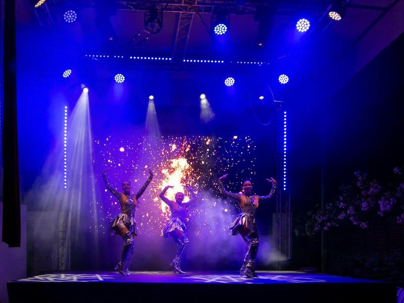 Bühne mit blauem Licht, Tänzer in Bewegung und funkelnden Lichteffekten im Hintergrund.